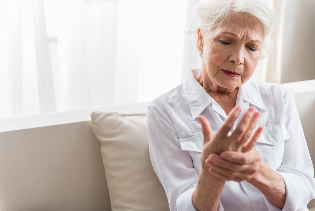 Die grauhaarige ältere Frau leidet an Arthrit is. Sie schaut auf ihre Hand und spürt furchtbare Schmerzen.