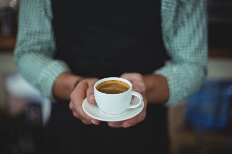 Mittelteil des Kellners, der im Café eine Tasse Kaffee hält