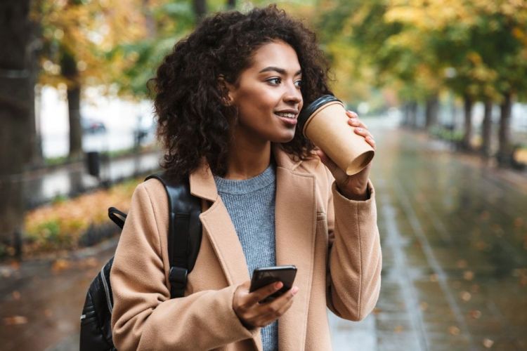 Schöne junge Afrikanerin mit Mobiltelefon in der Hand, trinkt Kaffee